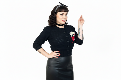 Woman wearing a black cardigan with a red and white design, black skirt, and headband on a white background