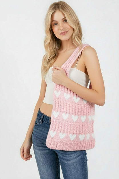 Woman holding a beige knitted bag with white heart patterns on a light pink background