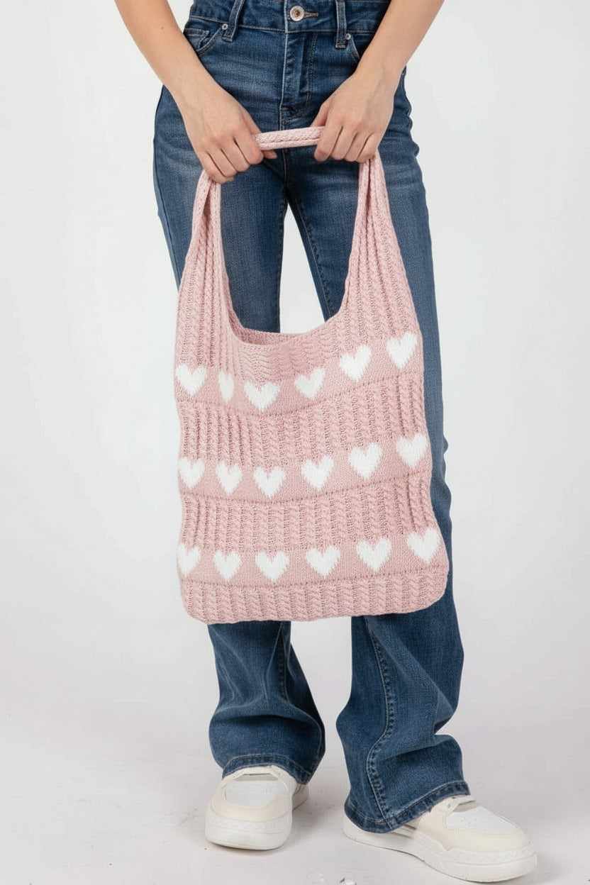 Person holding a knitted bag with with heart patterns against a light pink background