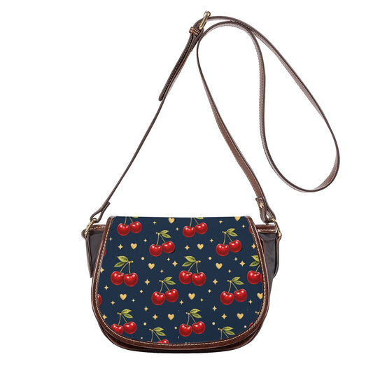 Front view of navy cherry print saddle bag crossbody with adjustable shoulder strap and brown trim.
