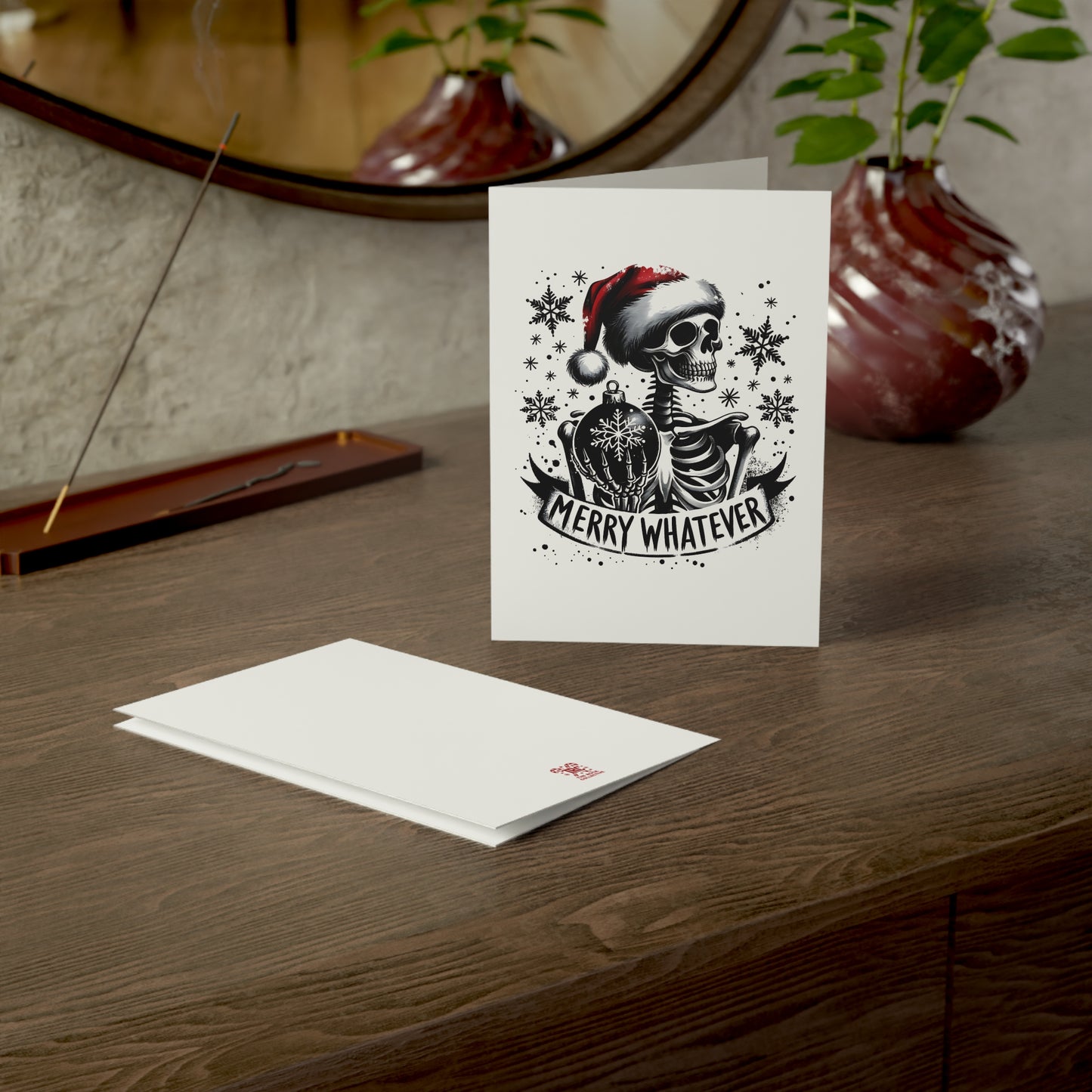 Greeting card with skeleton design and 'Merry Whatever' text on a wooden surface.
